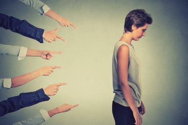 Concept of accusation guilty person girl. Side profile sad upset woman looking down many fingers pointing at her back isolated on grey office wall background. Human face expression emotion feeling